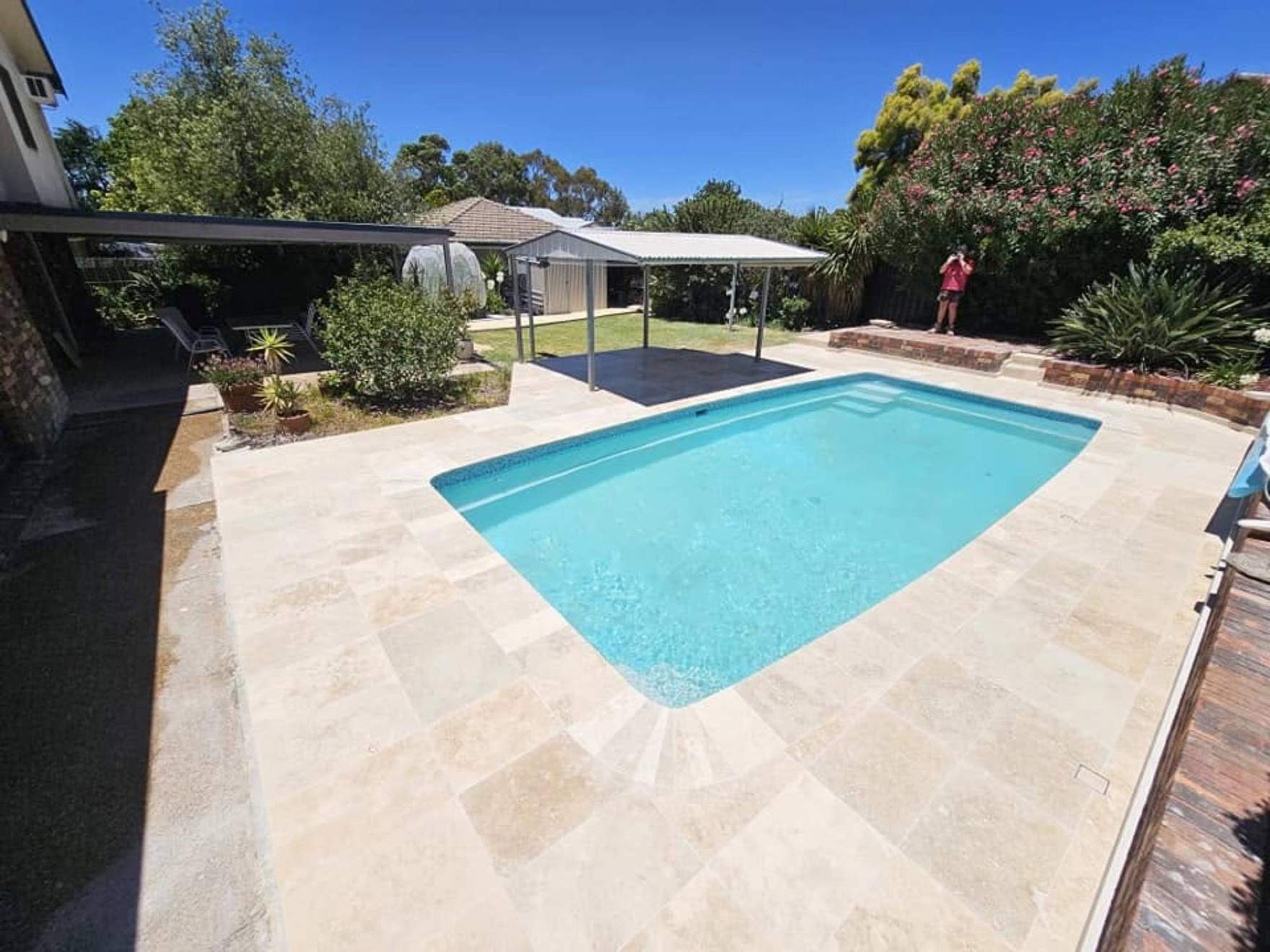 A pool with a paved surround and a covered patio behind