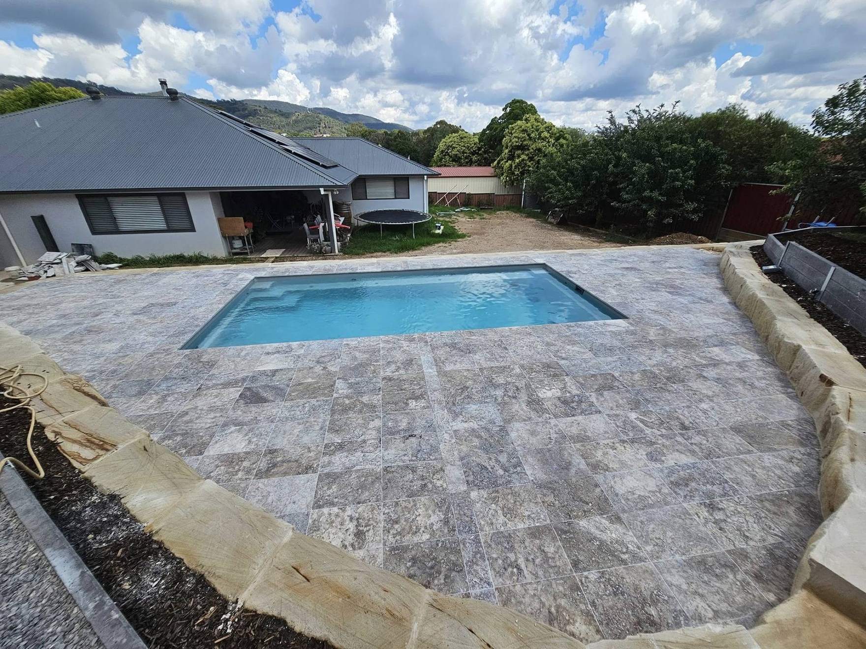 A pool and a wide stone-paved surround behind a country home