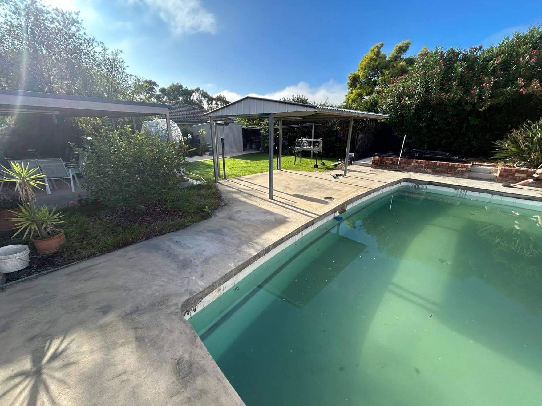 A pool and paved surround under a garden pergola