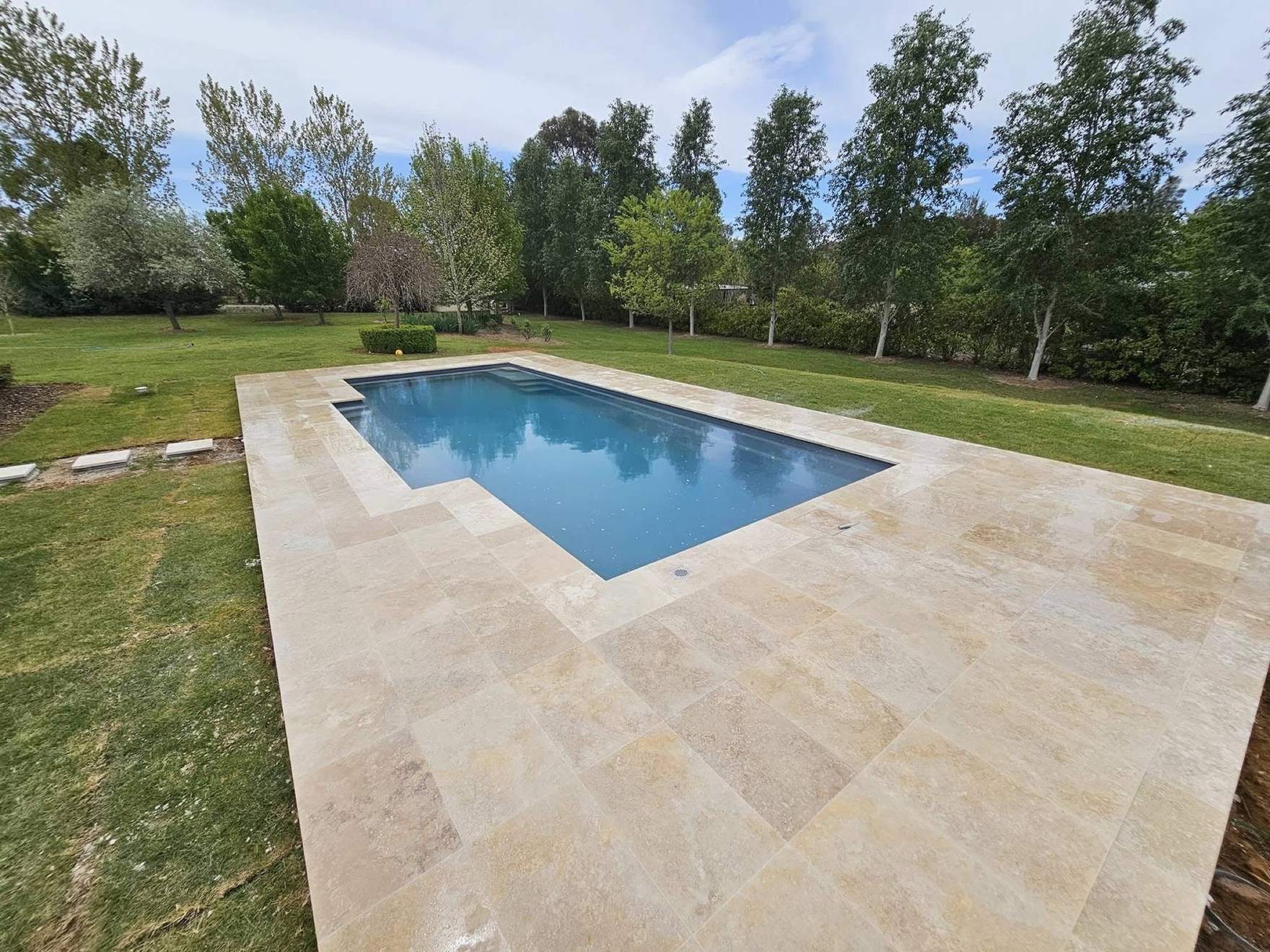A pool set in stone paving on a rural block lined with poplars