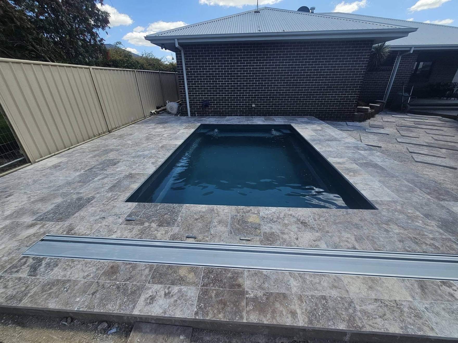A pool with a stone surround against a dark brick wall