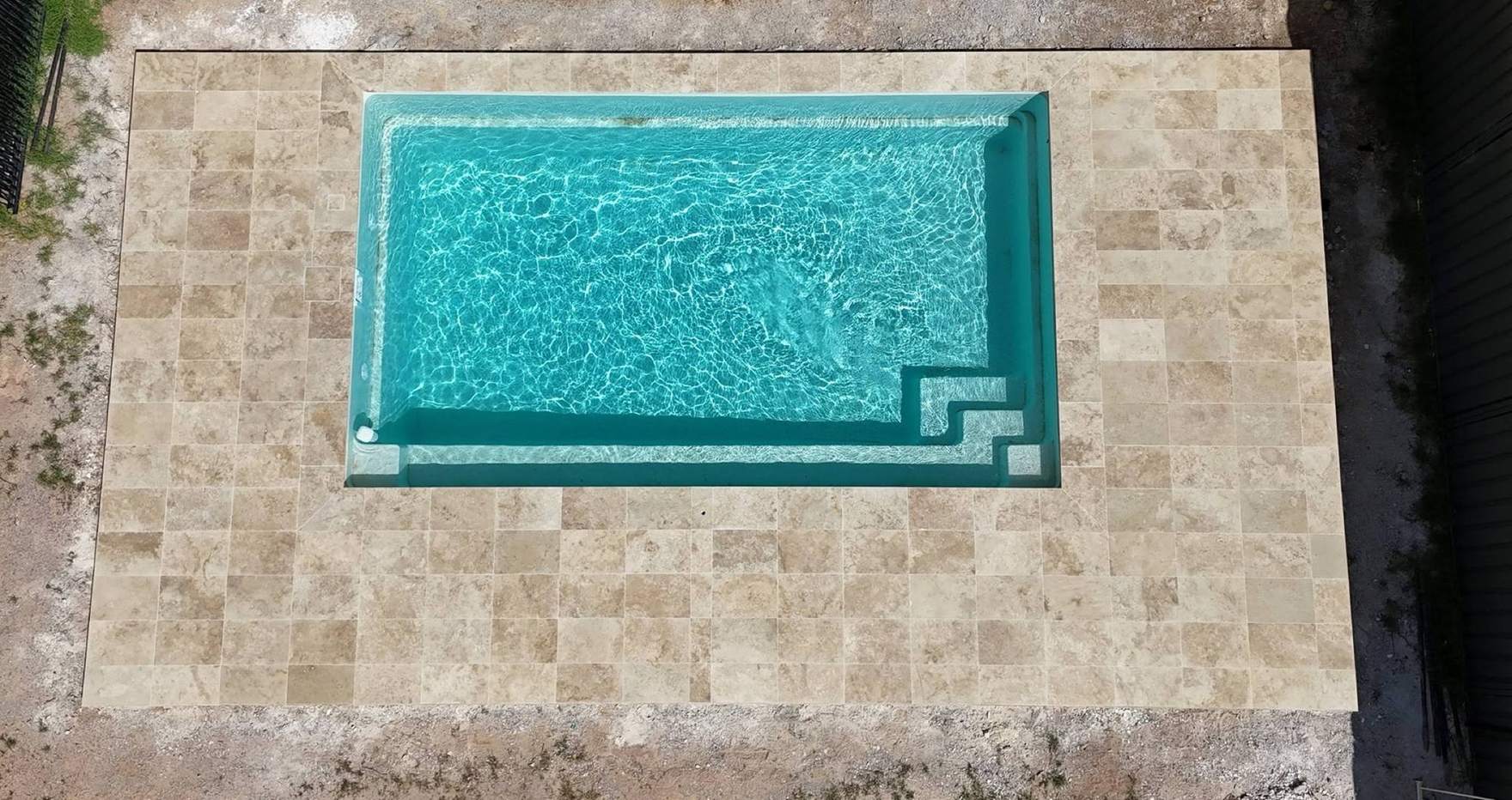 A pool framed on all sides by travertine paving, seen from above