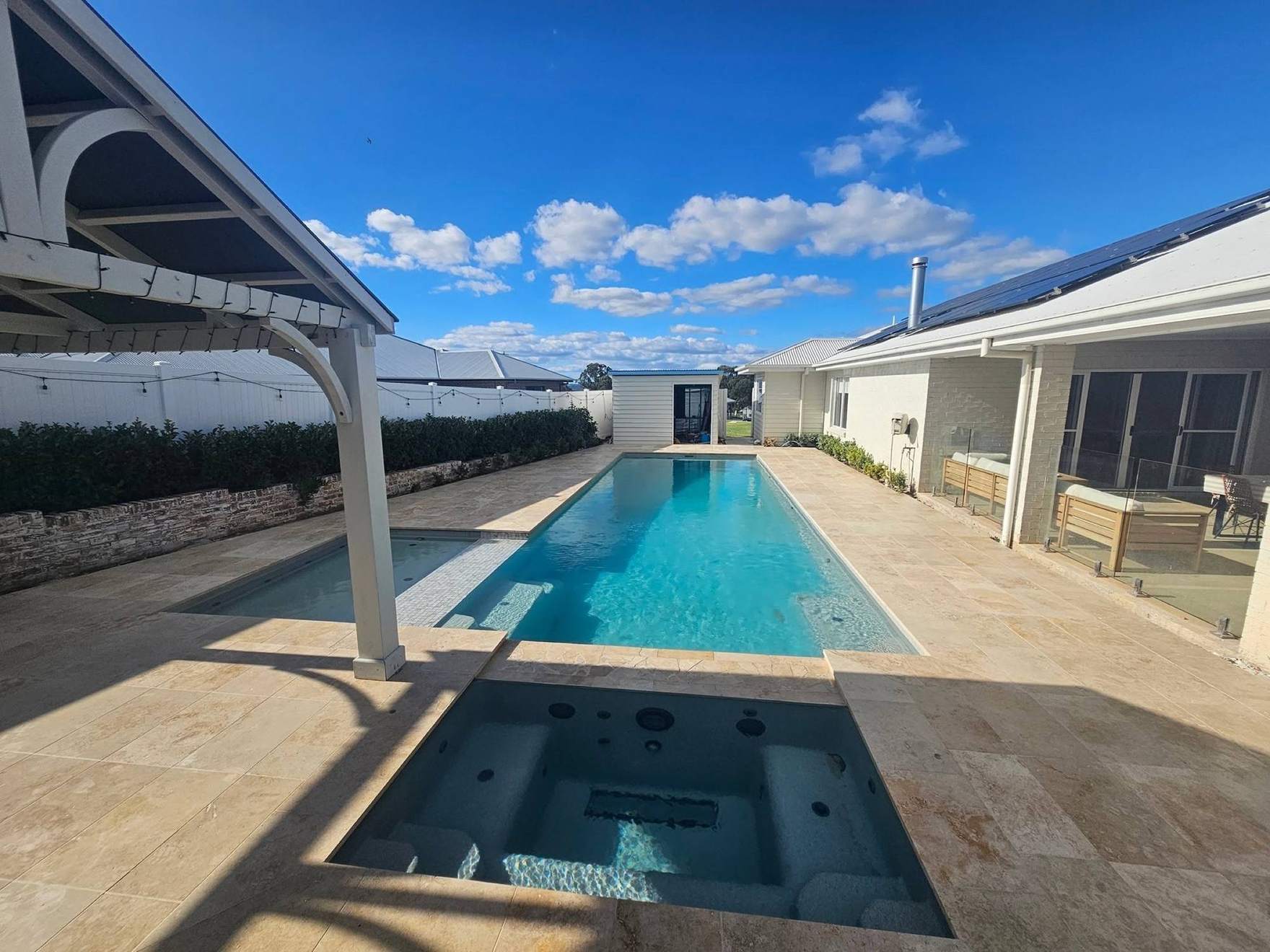 A swimming pool edged in travertine paving beside a home near Mudgee