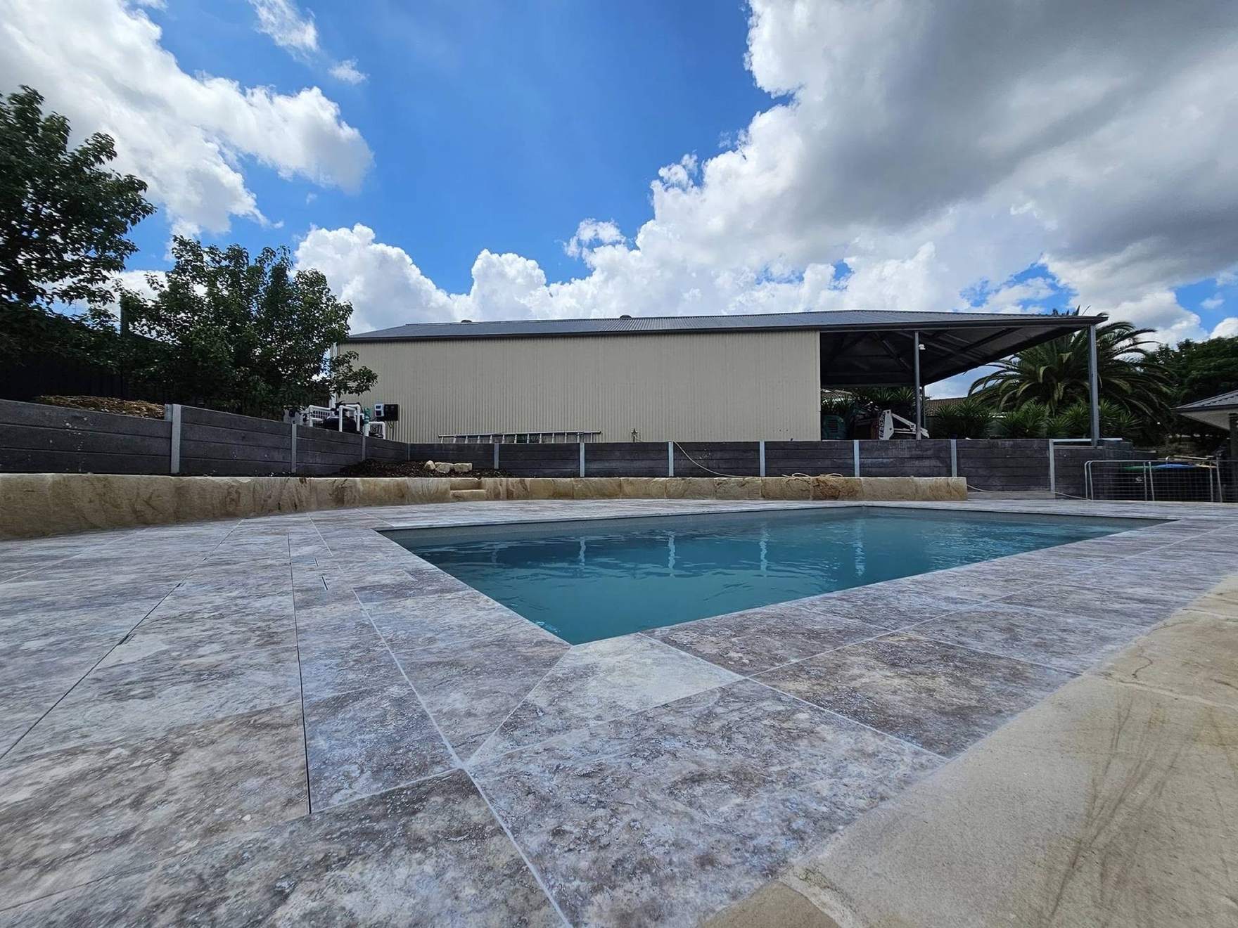 A pool set into a wide stone-paved surround under a cloudy sky