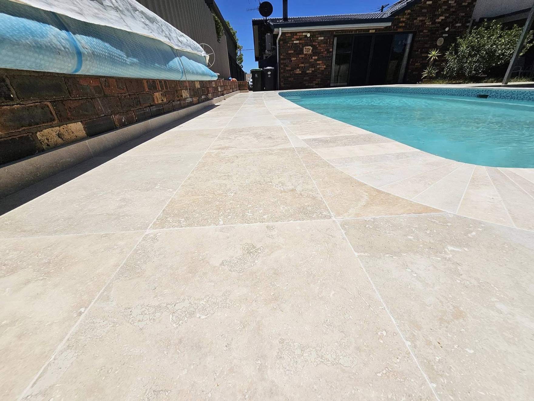 A wide travertine pool deck running out to the water’s edge