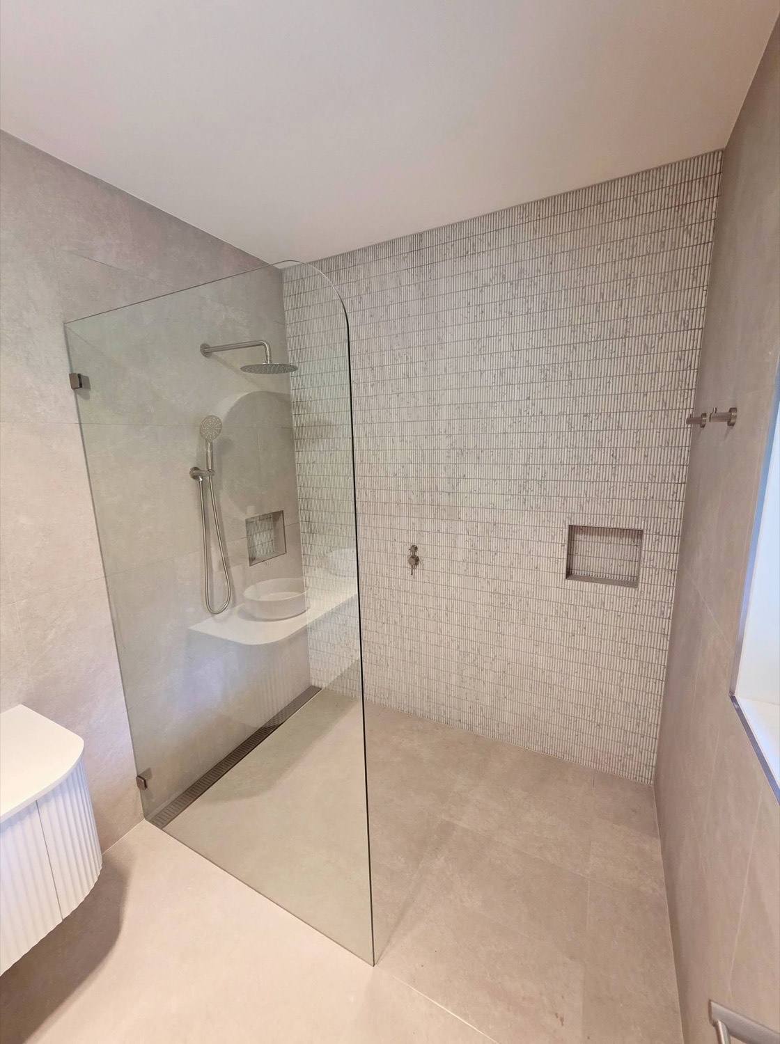 A tiled shower recess with a fine mosaic wall, a niche and a glass screen