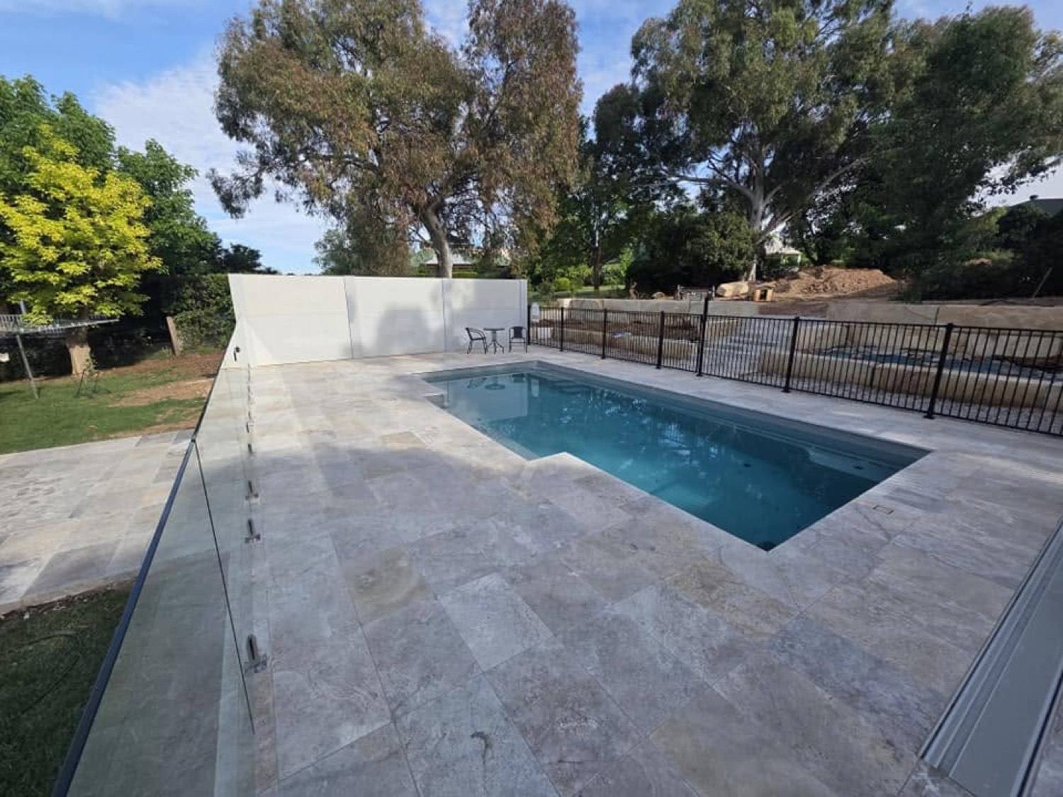 A pool with a fresh stone surround and glass fencing on a rural block