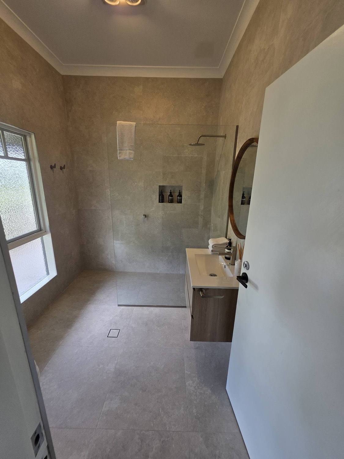 A shower part way through tiling, with the screen and vanity already in place
