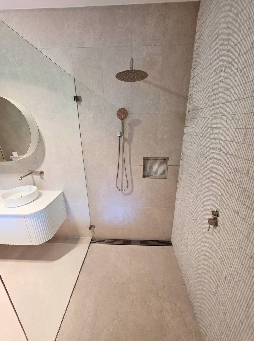 A tiled walk-in shower with a round mirror and a wall-hung vanity