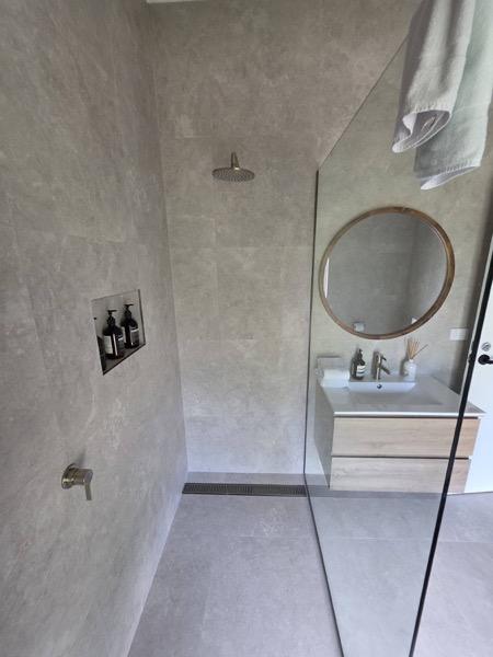 A bathroom with a round timber-framed mirror above a curved vanity
