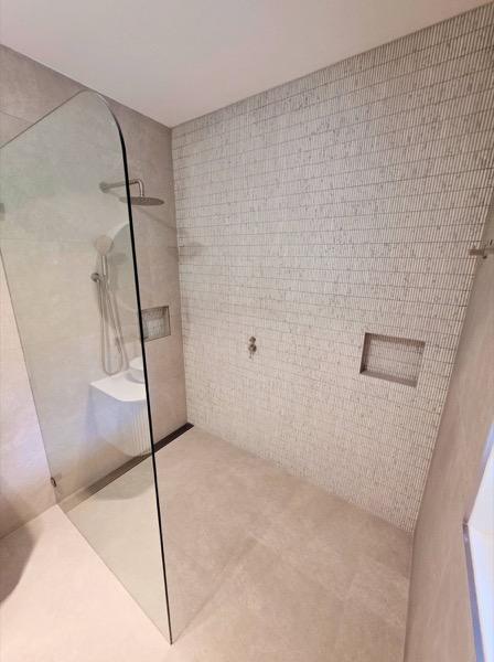 A shower wall in fine mosaic tile beside a frameless glass screen