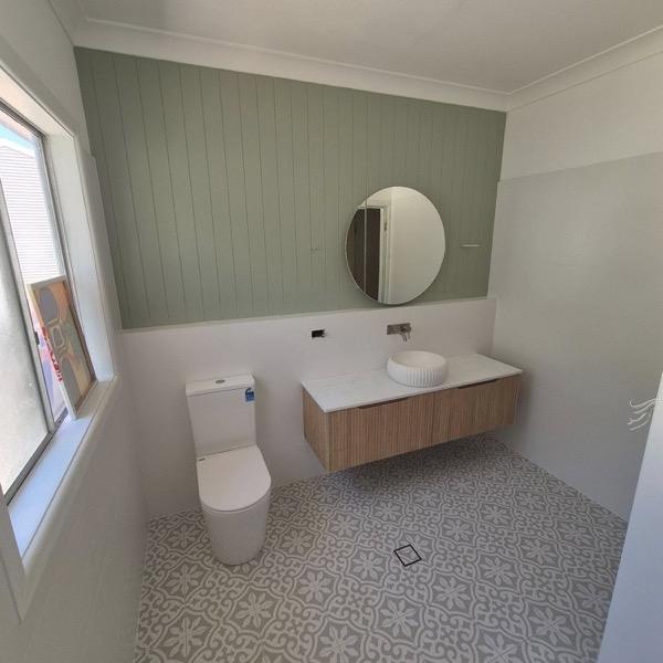 A bathroom vanity against a sage panelled wall on a patterned floor