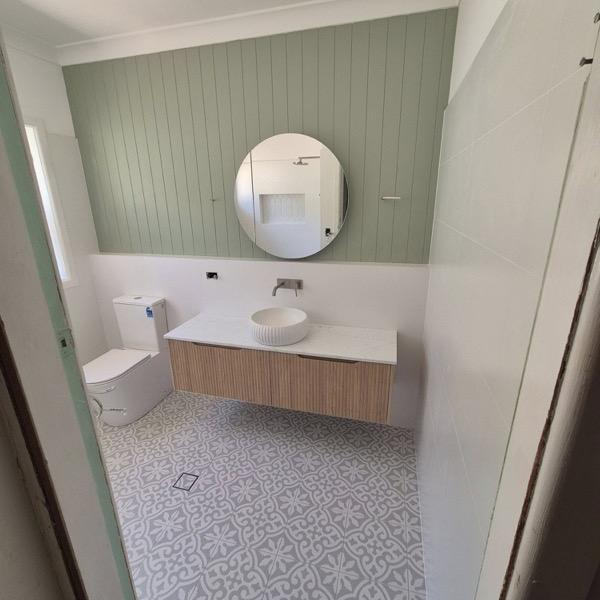 A wall-hung vanity and oval mirror over a patterned tiled floor