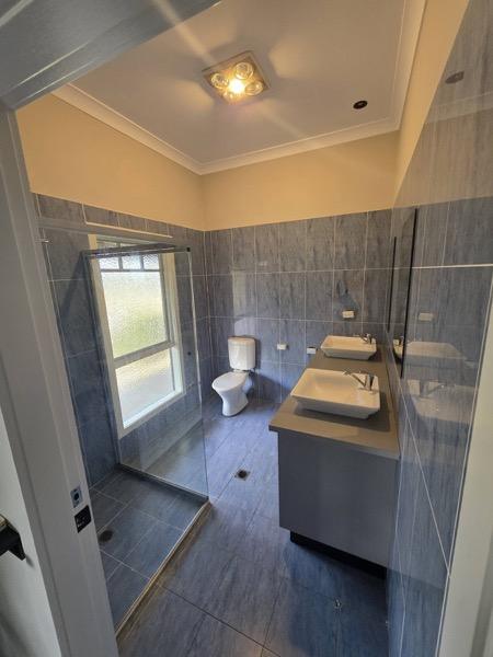 A grey-tiled bathroom with a double vanity and a shower behind glass