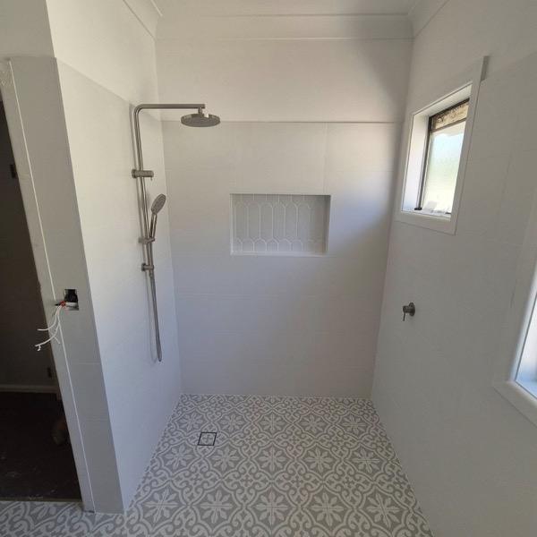A bathroom floor set in patterned tiles running to the shower