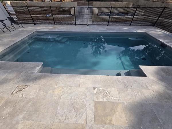A pool with stone coping and a paved surround beside a garden bed