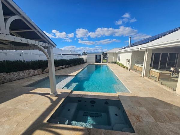A swimming pool edged in travertine paving beside a home