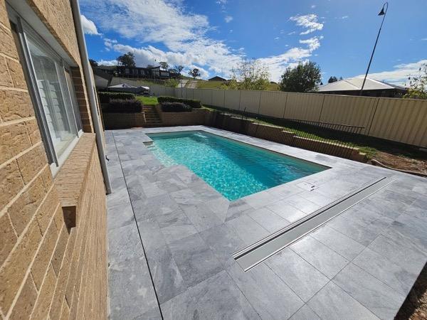 A pool with a stone surround along the side of a brick house