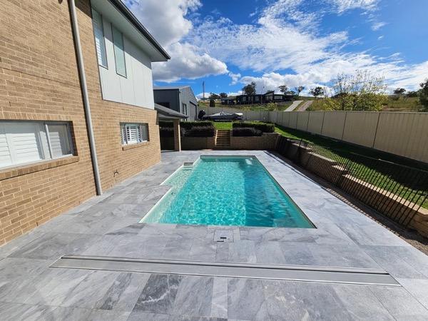 A rectangular pool edged in stone beside a brick home