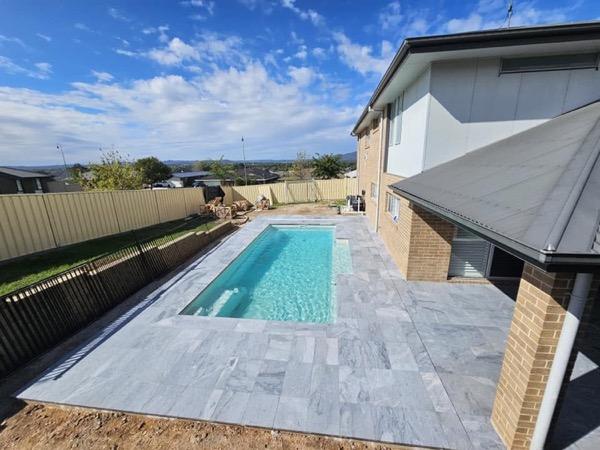 A pool with a wide stone surround and a colorbond fence behind