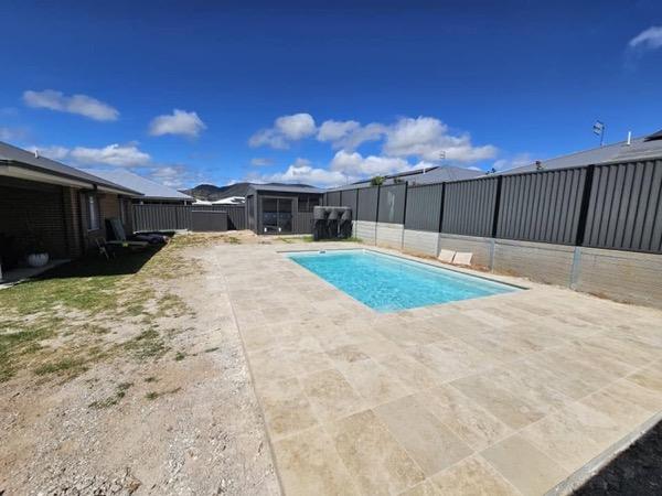 A pool and stone surround in a back yard bordered by a fence