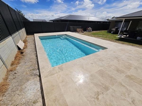 A pool with a stone paved surround and a low garden bed