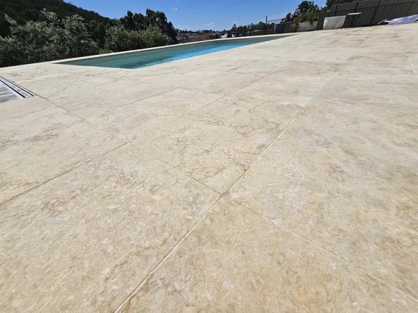A wide travertine paved deck running out to a pool edge