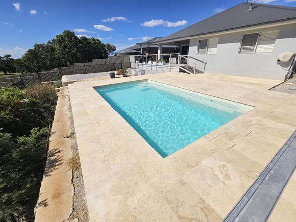 A pool and stone surround in front of a rendered house