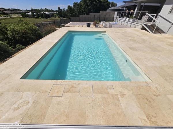 A long pool with stone coping and a paved entertaining area