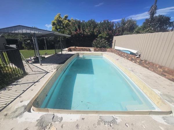 A pool beside a covered outdoor area with a stone surround