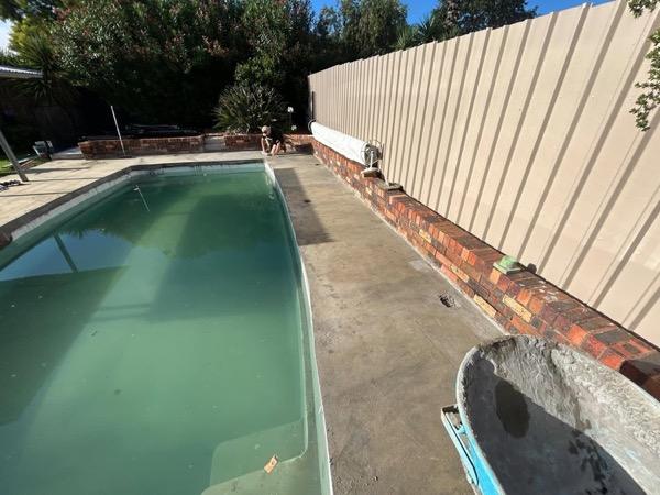 A pool with a paved surround against a brick retaining wall
