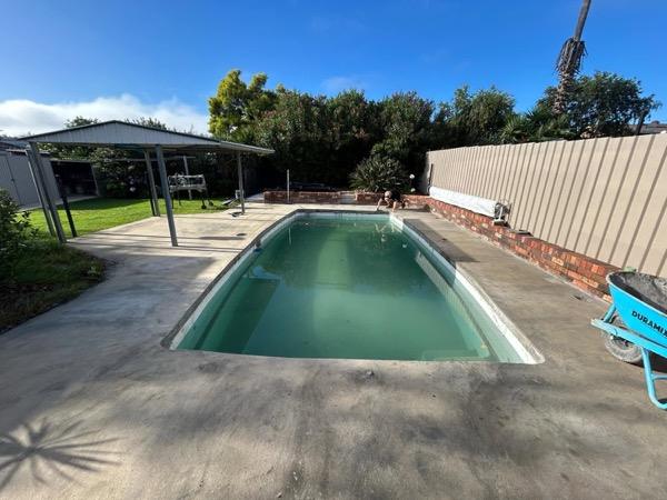 A pool with a stone surround beside a brick wall and a garden