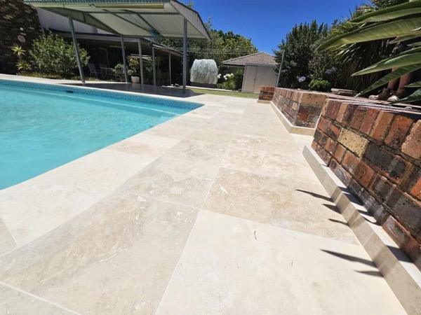 A pool with stone coping and a covered entertaining area alongside