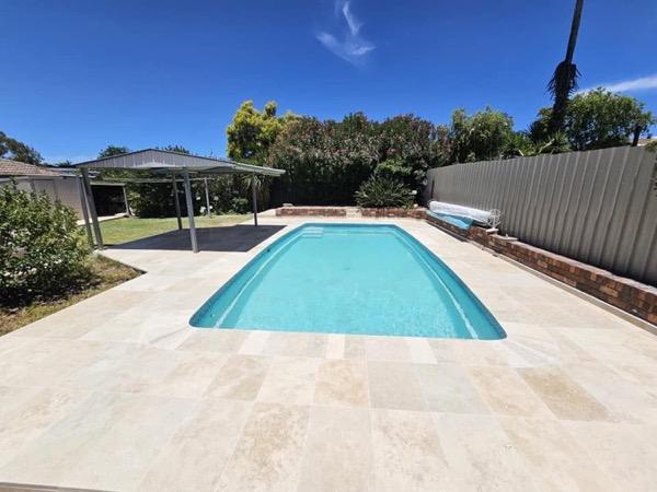 A pool with a paved surround and a covered patio behind