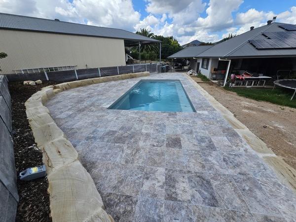 A stone pool surround with sandstone edging behind a home