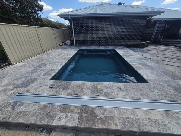 A pool with a stone surround against a dark brick wall