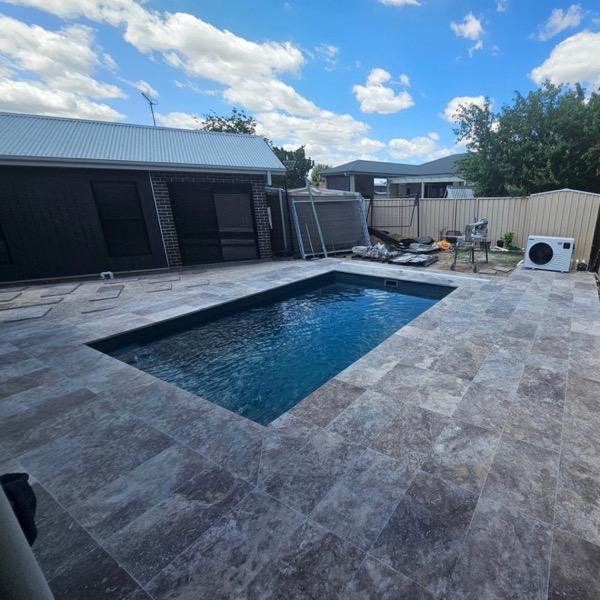A dark-tiled pool with a stone surround and a low brick wall
