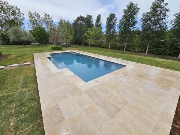 A pool set in stone paving on a rural block lined with poplars