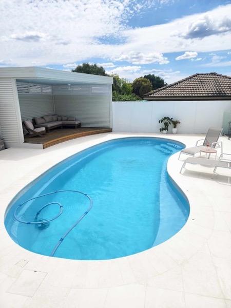 A curved pool with a paved surround beside a covered patio