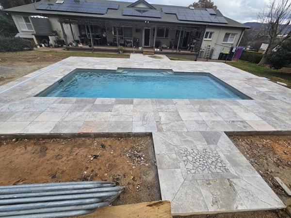 A pool with fresh stone paving and bare ground still to be finished