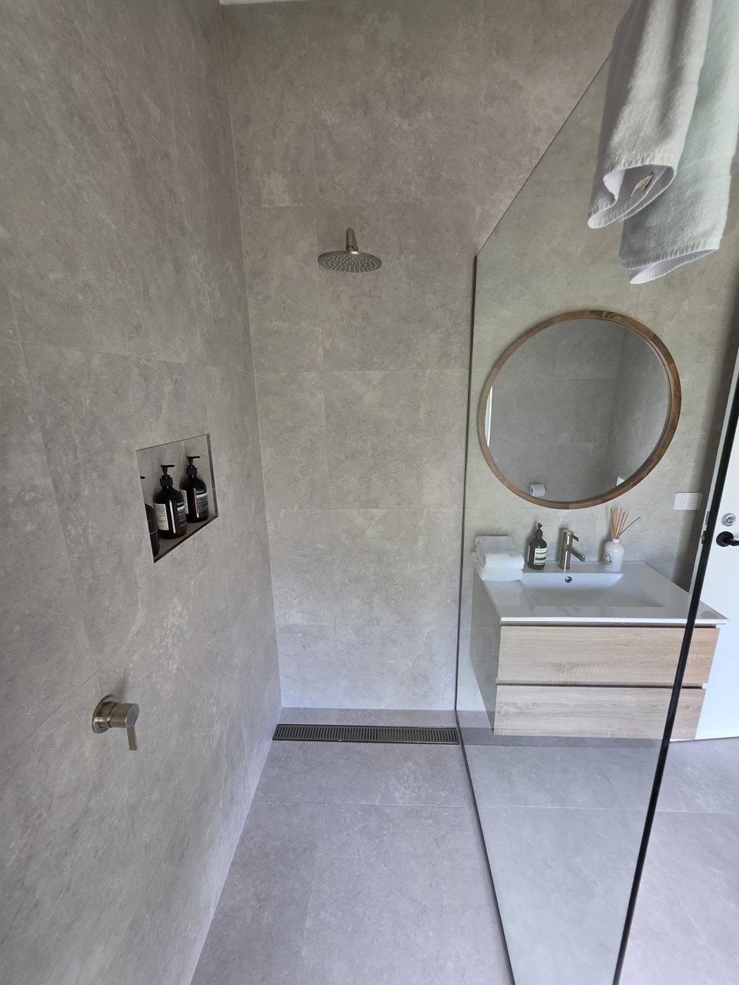 A tiled bathroom with a round mirror above a curved vanity
