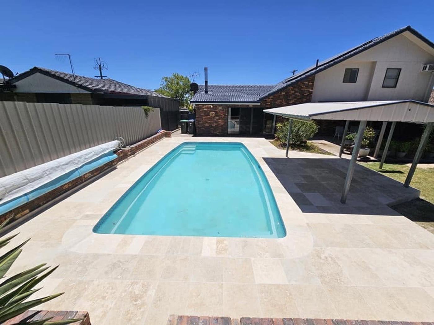 A pool ringed by stone paving in a back yard